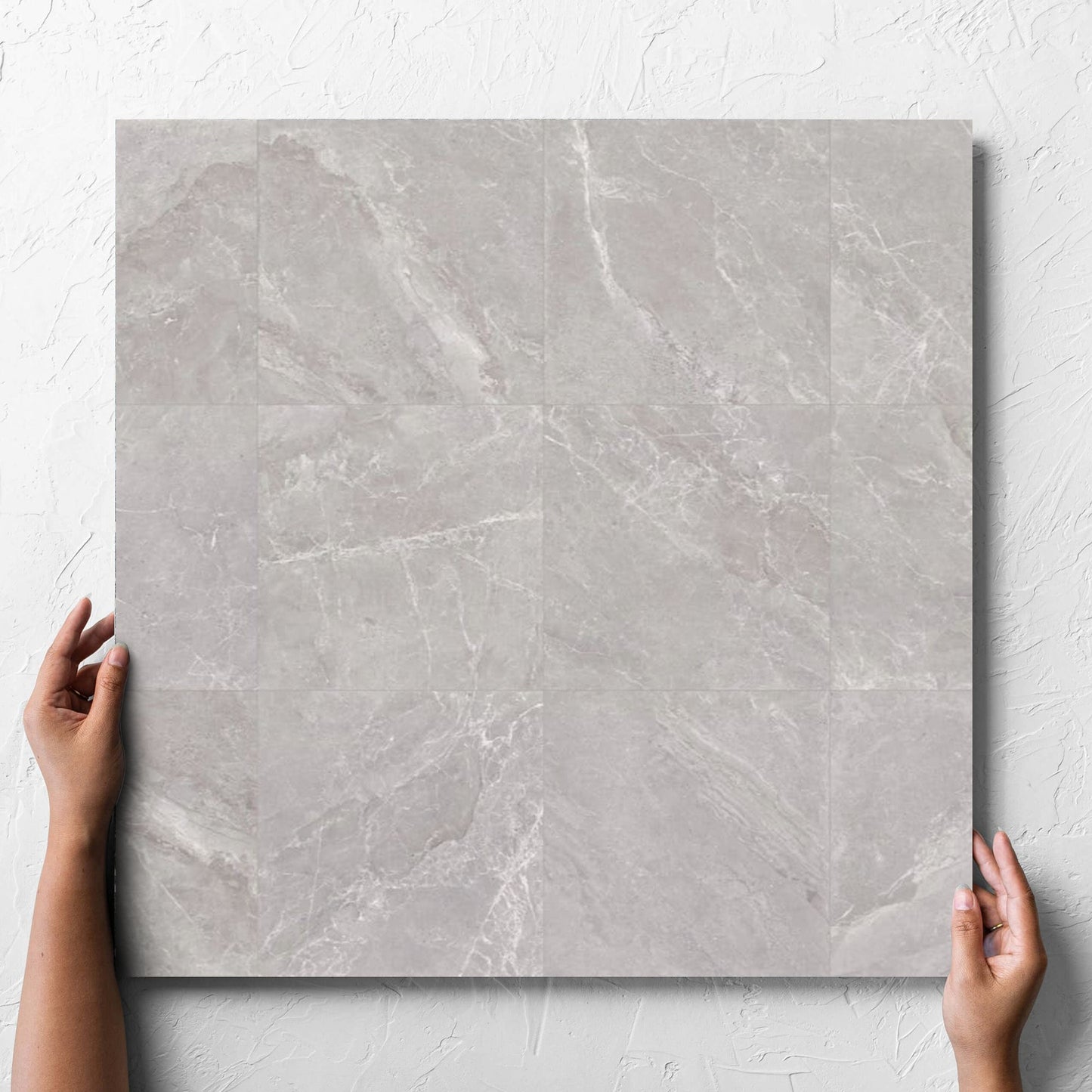 Hand holding a single Alpen Stone Grey 600x600mm tile against a white rendered wall, showing the tile surface