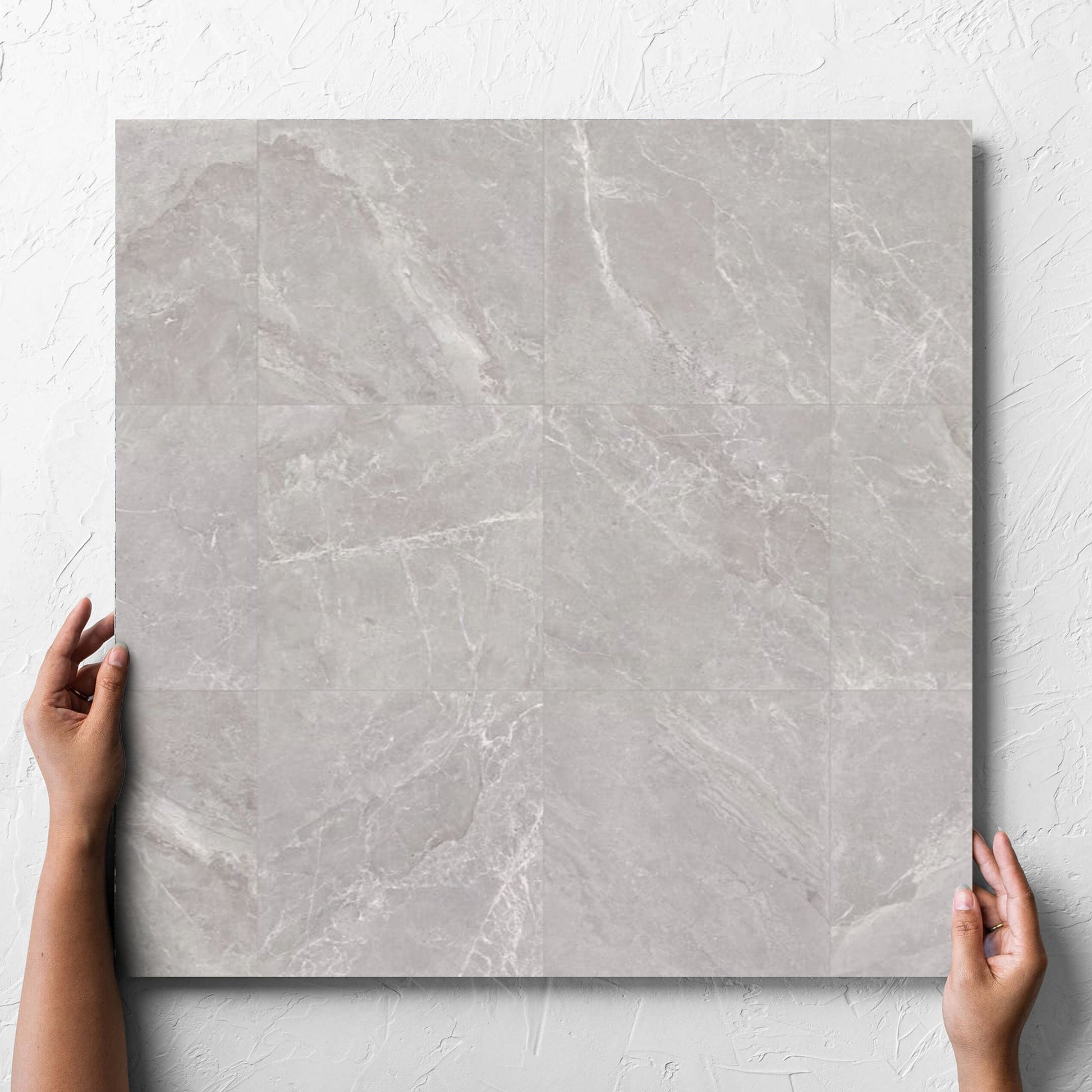 Hand holding a single Alpen Stone Grey 600x600mm tile against a white rendered wall, showing the tile surface