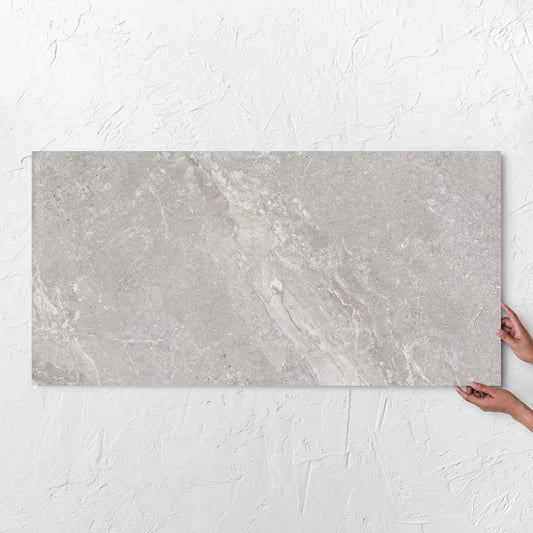 Hands holding a Alpen Stone Grey Lappato 600x1200mm tile against a white rendered wall, showing the tile surface
