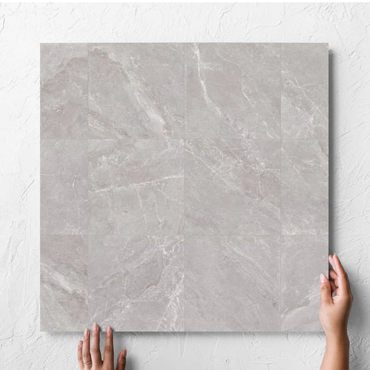 Hand holding a single Alpen Stone Grey Lappato 600x600mm tile against a white rendered wall, showing the tile surface