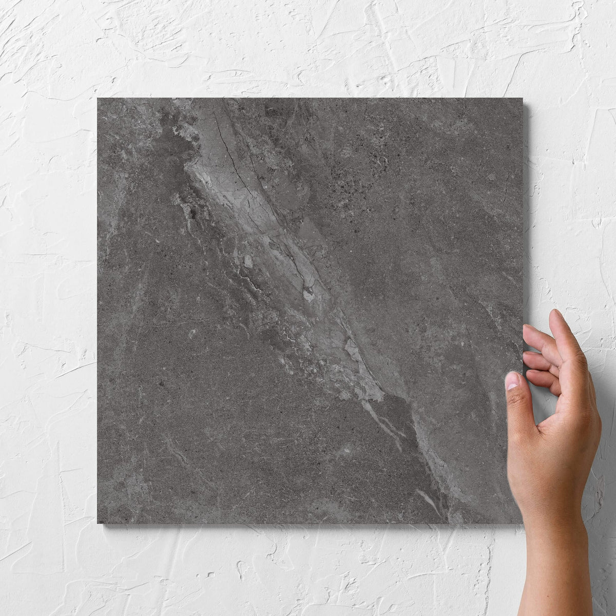 Hand holding a single Alpen Stone Smoke 300x300mm tile against a white rendered wall, showing the smoke surface