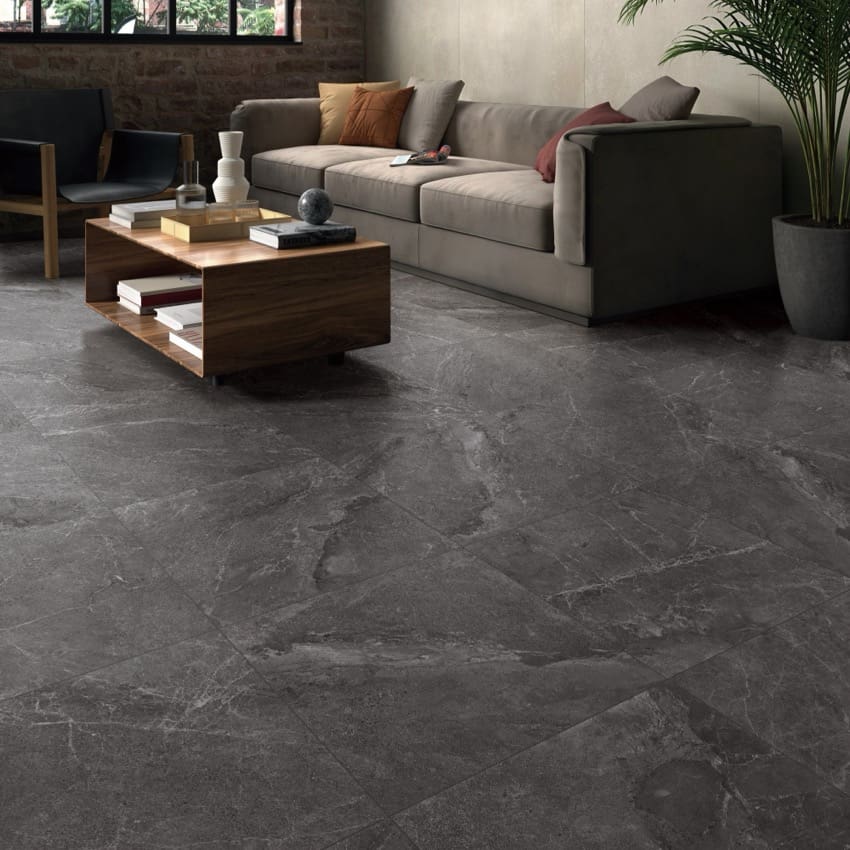Alpen Stone Smoke 300x600mm dark grey marble-effect floor tiles installed in a modern living room with sofa and wooden coffee table.