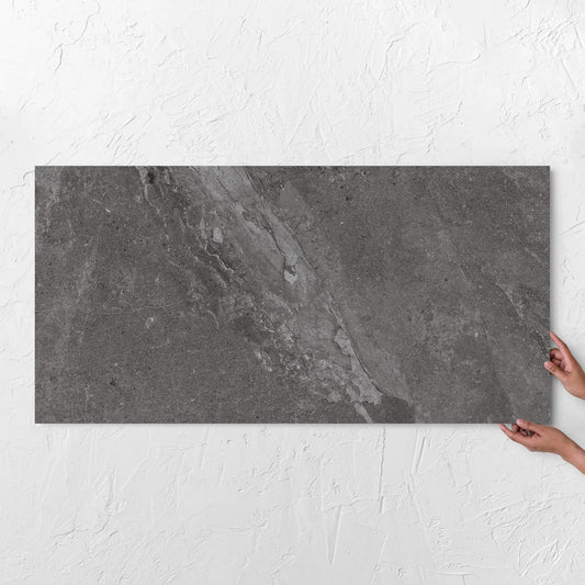 Hands holding a Alpen Stone Smoke 600x1200mm tile against a white rendered wall, showing the smoke surface