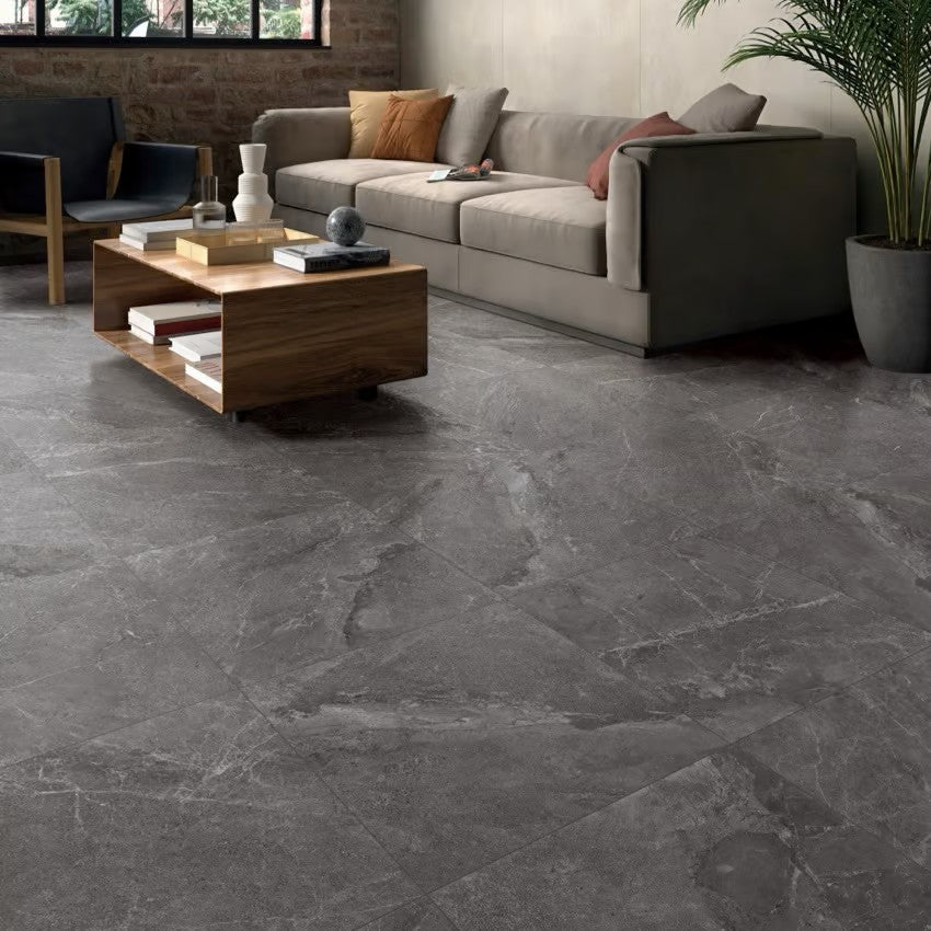 Alpen Stone Smoke 600x600mm dark grey marble-effect floor tiles installed in a modern living room with a grey sofa and wooden coffee table.