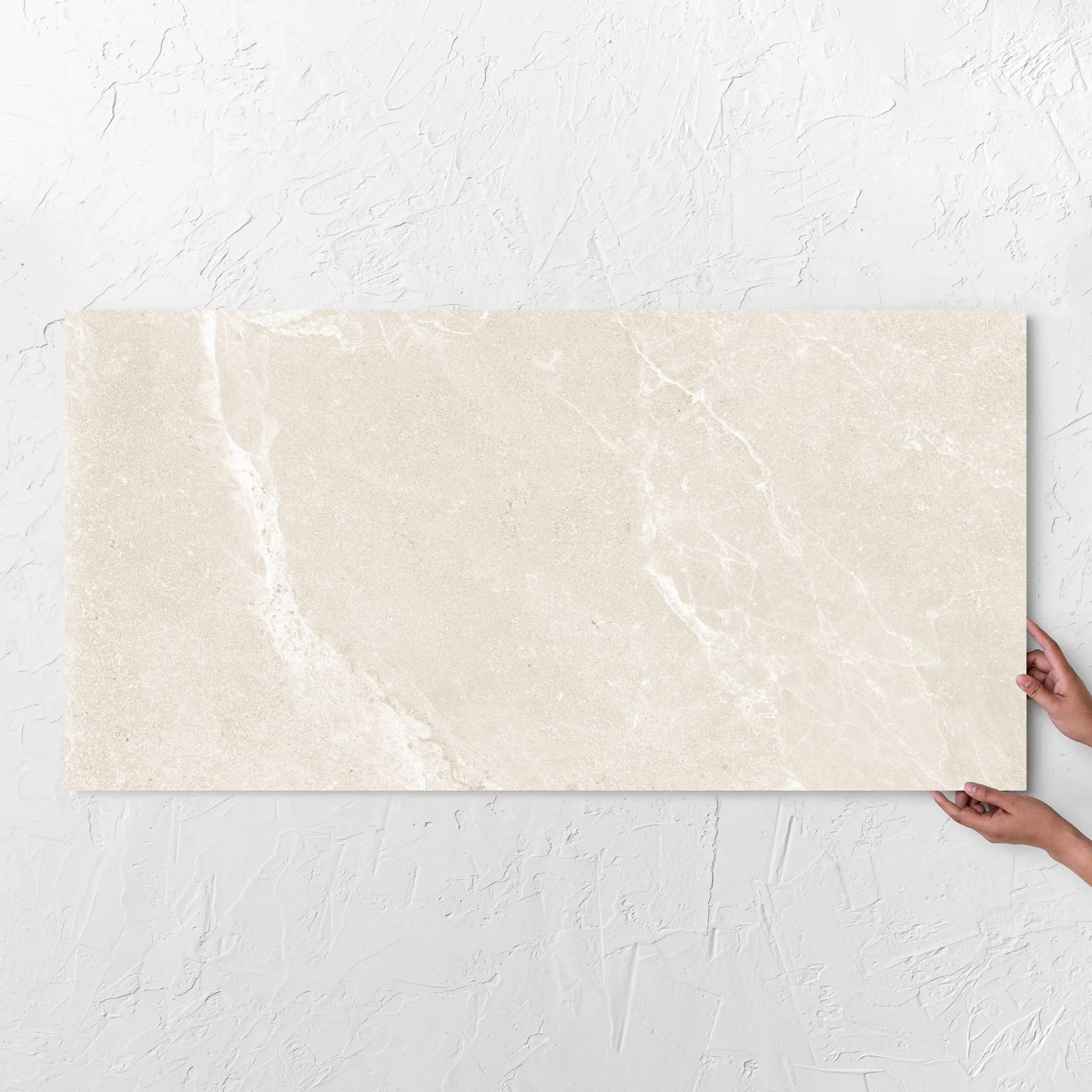 Hands holding a Alpen Stone Warm 600x1200mm tile against a white rendered wall, showing the tile surface