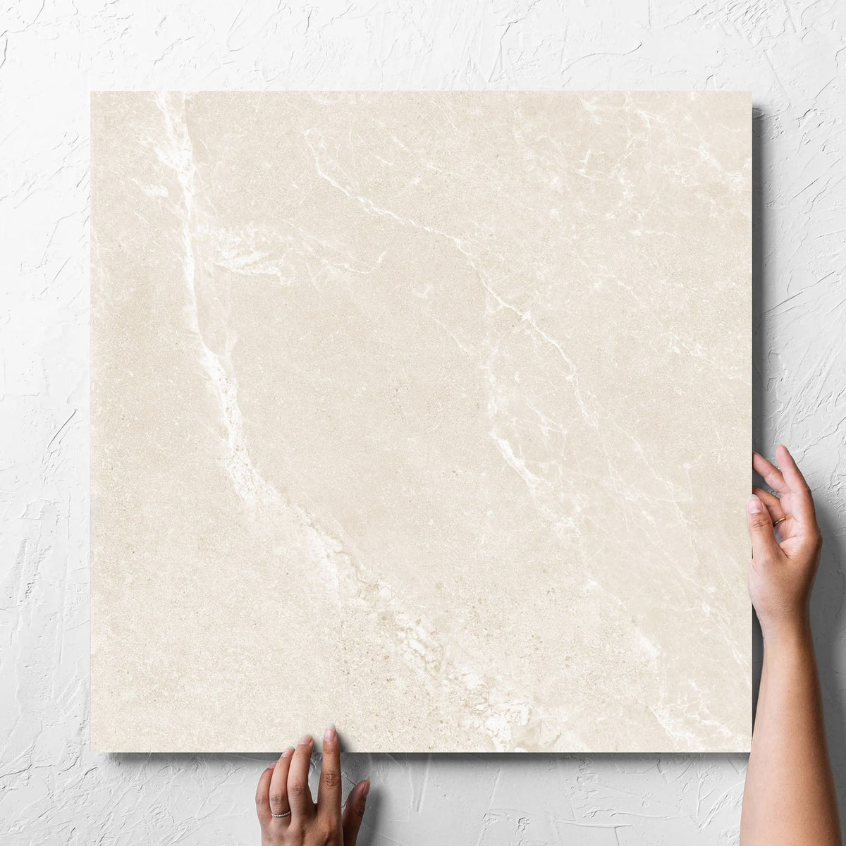 Hand holding a single Alpen Stone Warm Lappato 600x600mm tile against a white rendered wall, showing the tile surface