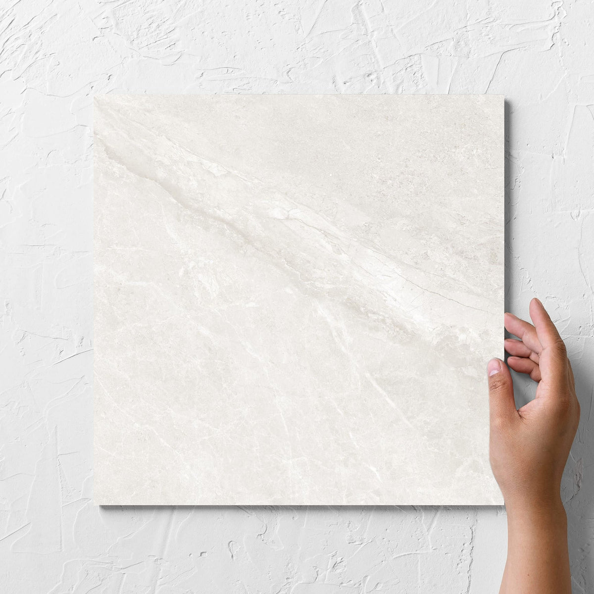 Hand holding a single Alpen Stone White 300x300mm tile against a white rendered wall, showing the white surface