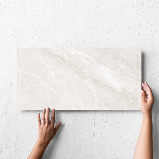 Hand holding a single Alpen Stone White 300x600mm tile against a white rendered wall, showing the white surface