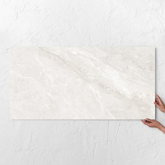 Hands holding a Alpen Stone White 600x1200mm tile against a white rendered wall, showing the white surface