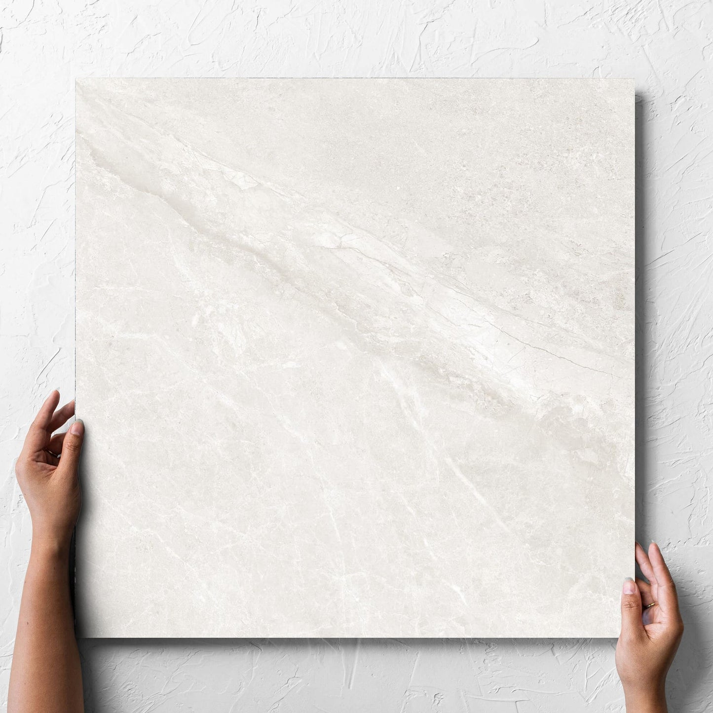 Hand holding a single Alpen Stone White 600x600mm tile against a white rendered wall, showing the tile surface