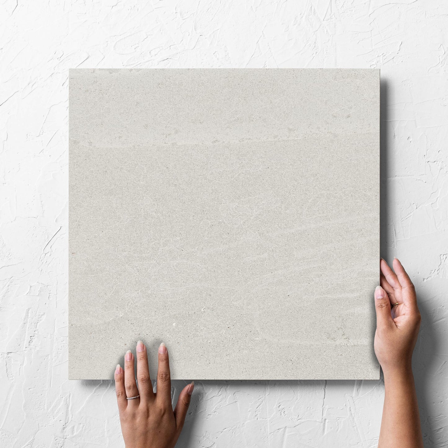 Hand holding a single Alps Light Grey Matt 450x450mm tile against a white rendered wall, showing the tile surface