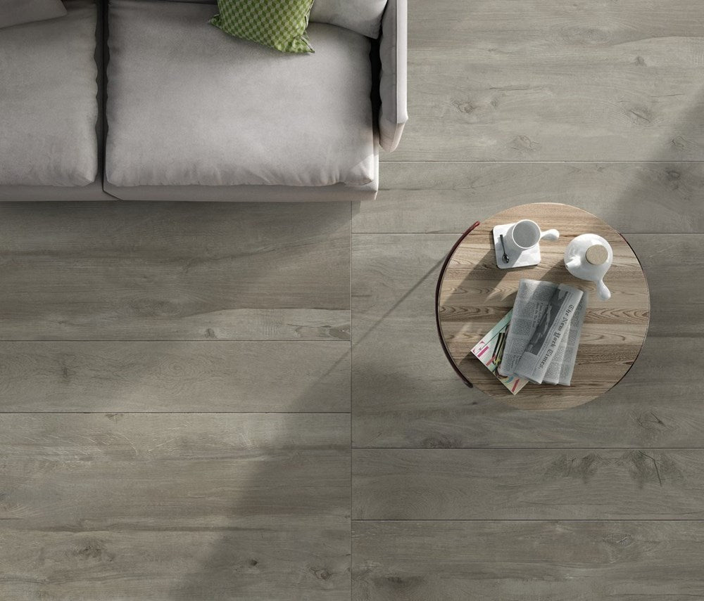 Amazon Light Grey Matt 200x1200mm wood-effect floor tiles installed in a modern living room with a grey sofa and round coffee table.
