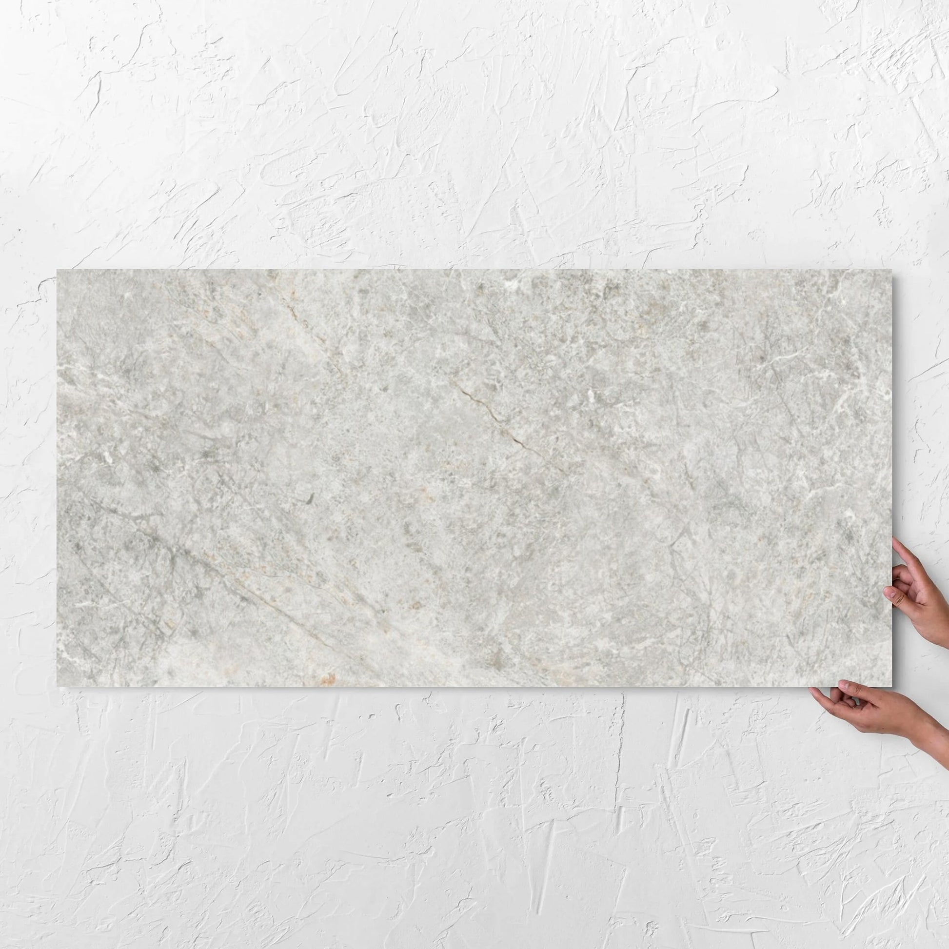 Hands holding a Antalya Beige Amber 600x1200mm tile against a white rendered wall, showing the matt surface