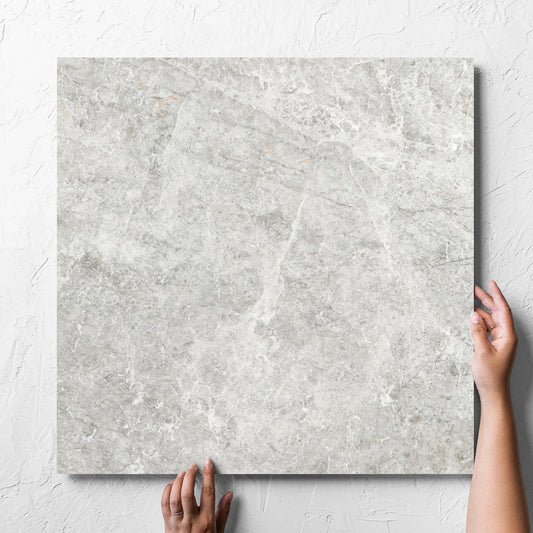 Hand holding a single Antalya Beige Amber 600x600mm tile against a white rendered wall, showing the matt surface