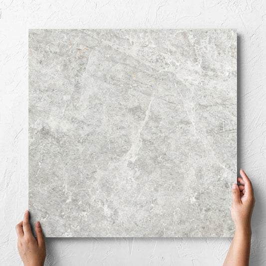 Hand holding a single Antalya Beige Matt 600x600mm tile against a white rendered wall, showing the matt surface