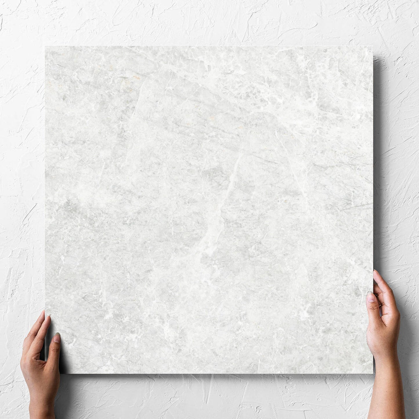 Hand holding a single Antalya Bianco Amber 600x600mm tile against a white rendered wall, showing the matt surface