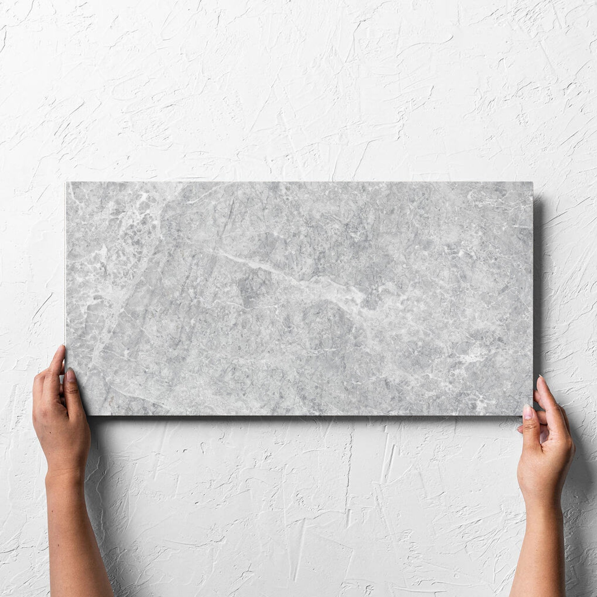 Hand holding a single Antalya Silver Matt 300x600mm tile against a white rendered wall, showing the matt surface