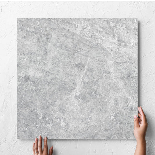 Hand holding a single Antalya Silver Matt 600x600mm tile against a white rendered wall, showing the matt surface