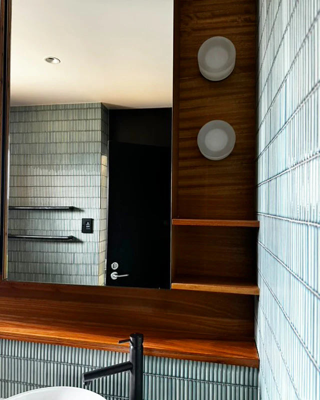 Antique Green Gloss Porcelain Glazed KitKat 12x92mm tiles covering a bathroom vanity wall beside a warm timber mirror frame and wood shelf unit.