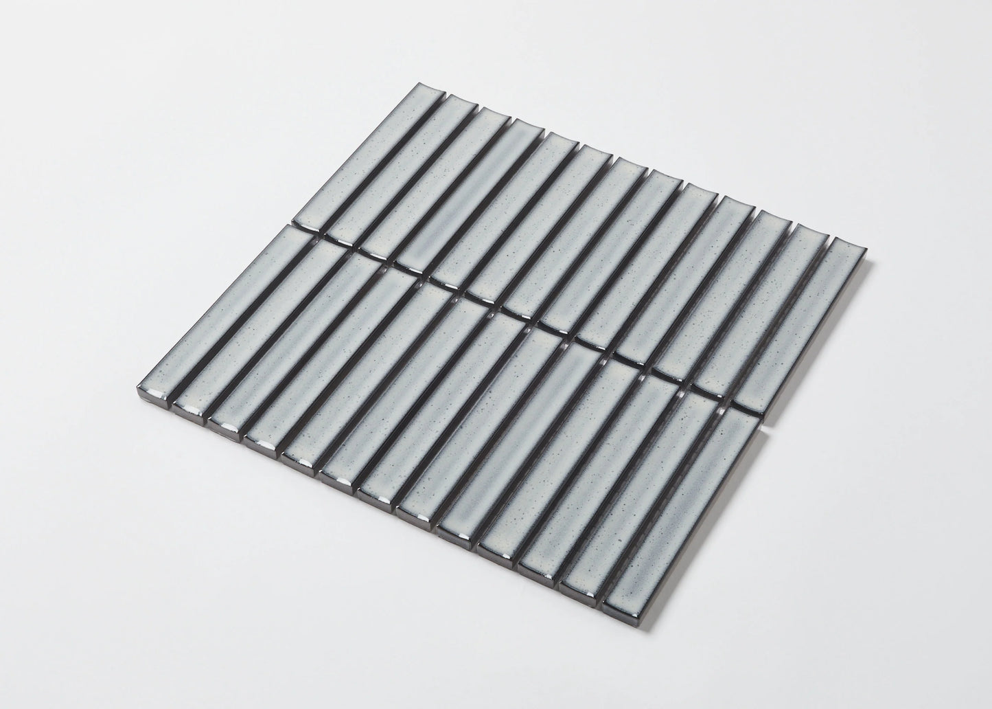 Pack shot of Antique Grey Speckled Gloss Concave Porcelain Glazed Finger 20x145mm tiles arranged in a square sheet, showing their pale grey glazed concave surface with subtle speckled texture.