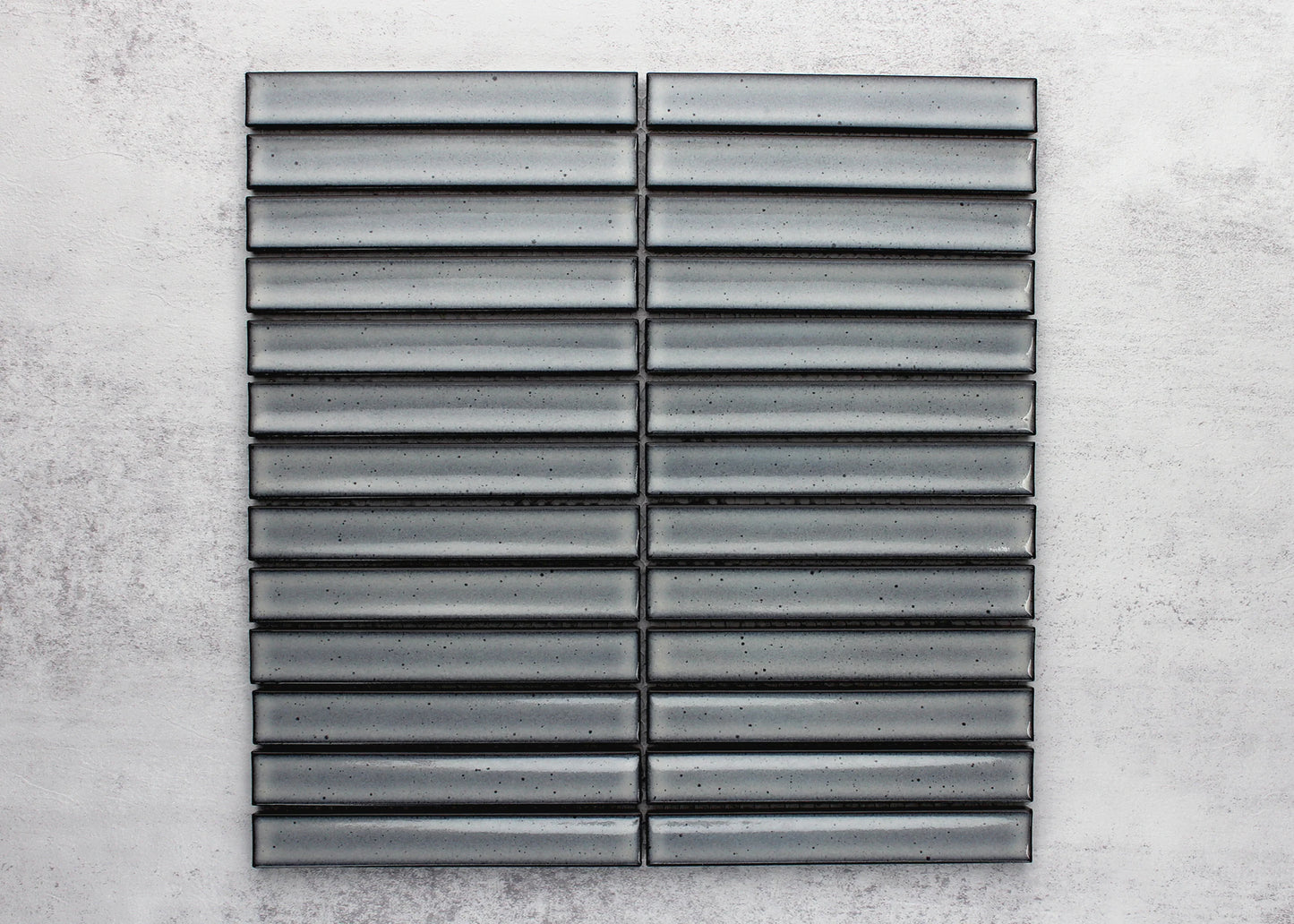 Pack shot of Antique Grey Speckled Gloss Concave Porcelain Glazed Finger 20x145mm tiles arranged in a stacked horizontal grid pattern showing their grey glazed concave surface with dark speckled detailing.