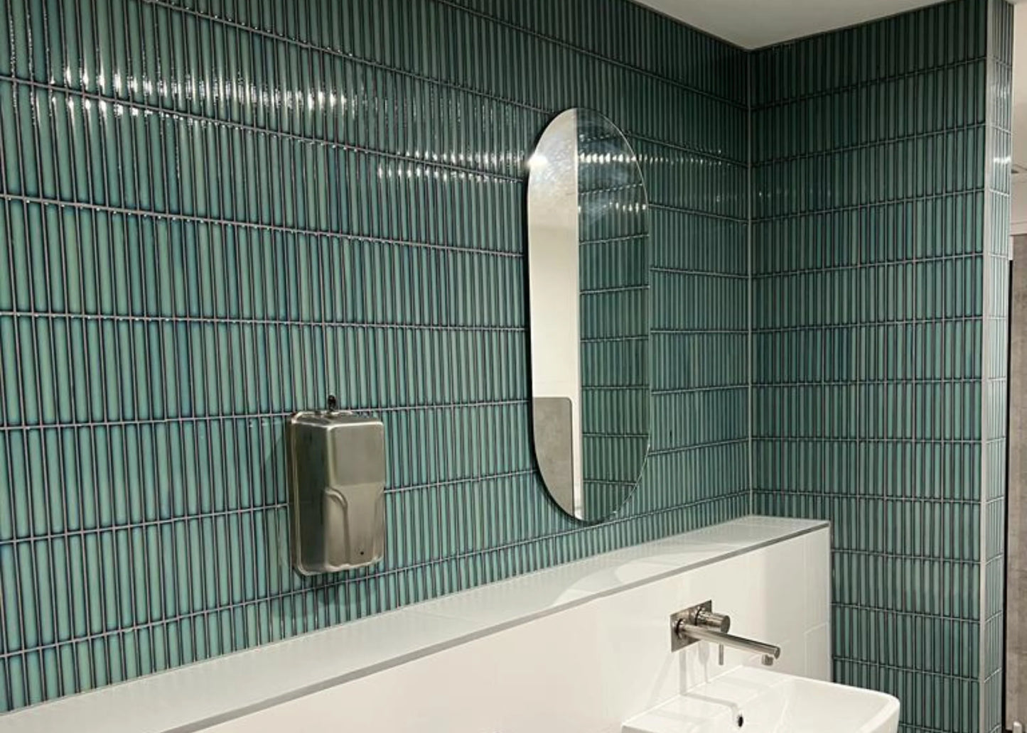Antique Medium Green Gloss Concave Porcelain Glazed Finger 20x145mm tiles installed floor-to-ceiling in a modern bathroom featuring an oval mirror and white vanity basin.