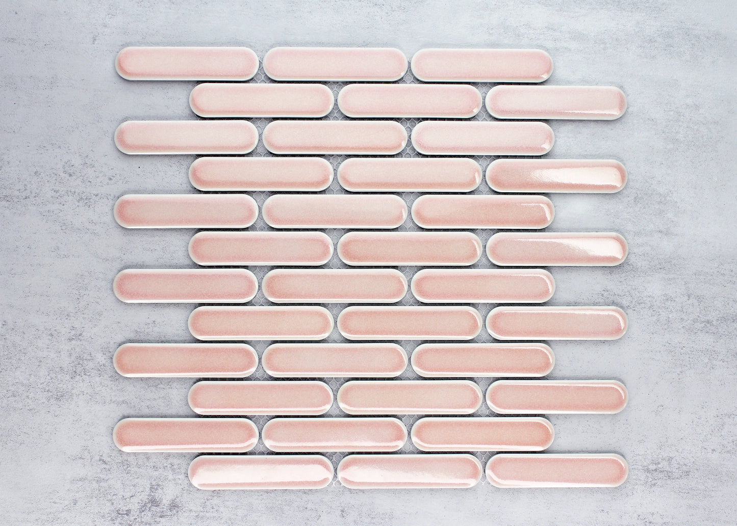 Flat-lay close-up of Antique Pink Gloss Round Head Finger Glazed Mosaic 23x93mm tiles arranged in staggered rows showing soft pink glaze and rounded oblong shape.