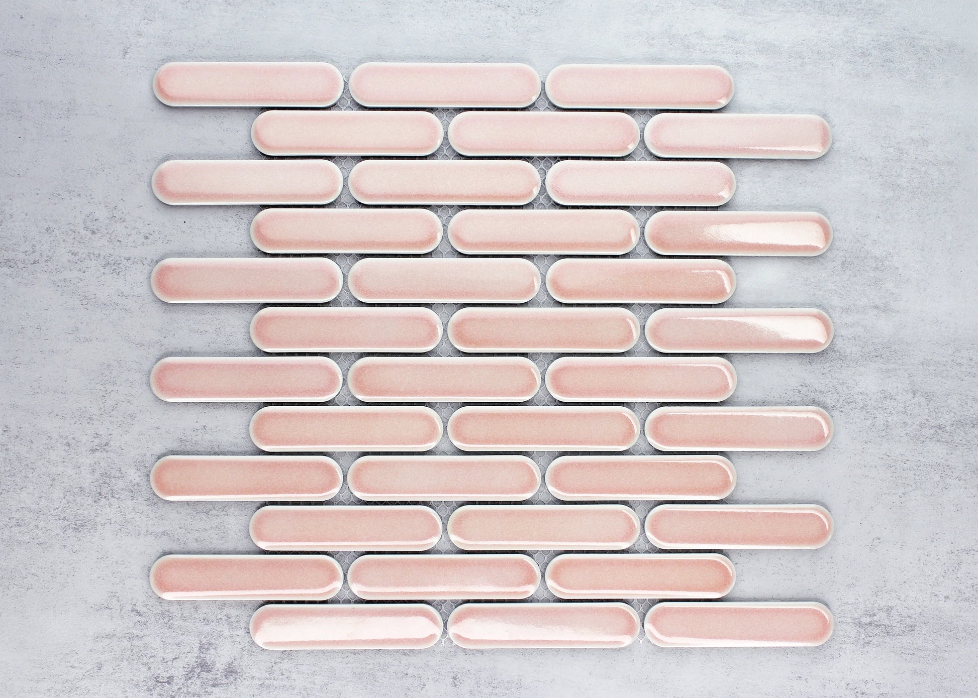 Flat-lay close-up of Antique Pink Gloss Round Head Finger Glazed Mosaic 23x93mm tiles arranged in staggered rows showing soft pink glaze and rounded oblong shape.