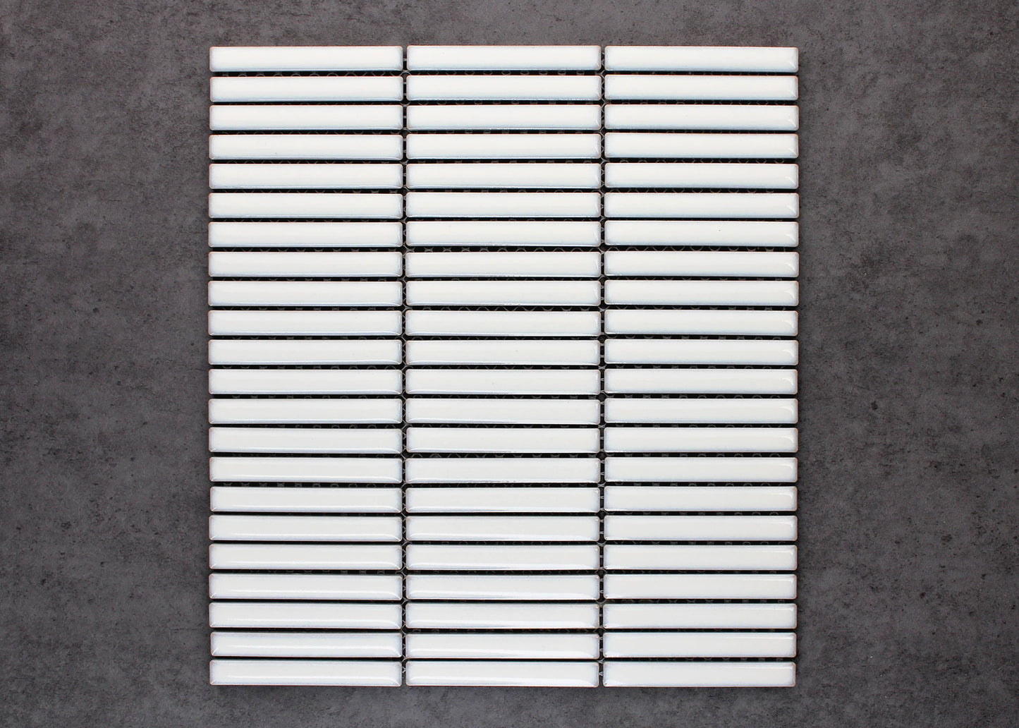 A flat-lay pack shot of Antique White Gloss Porcelain Glazed KitKat 12x92mm tiles arranged in three stacked mesh-mounted columns against a grey concrete background.