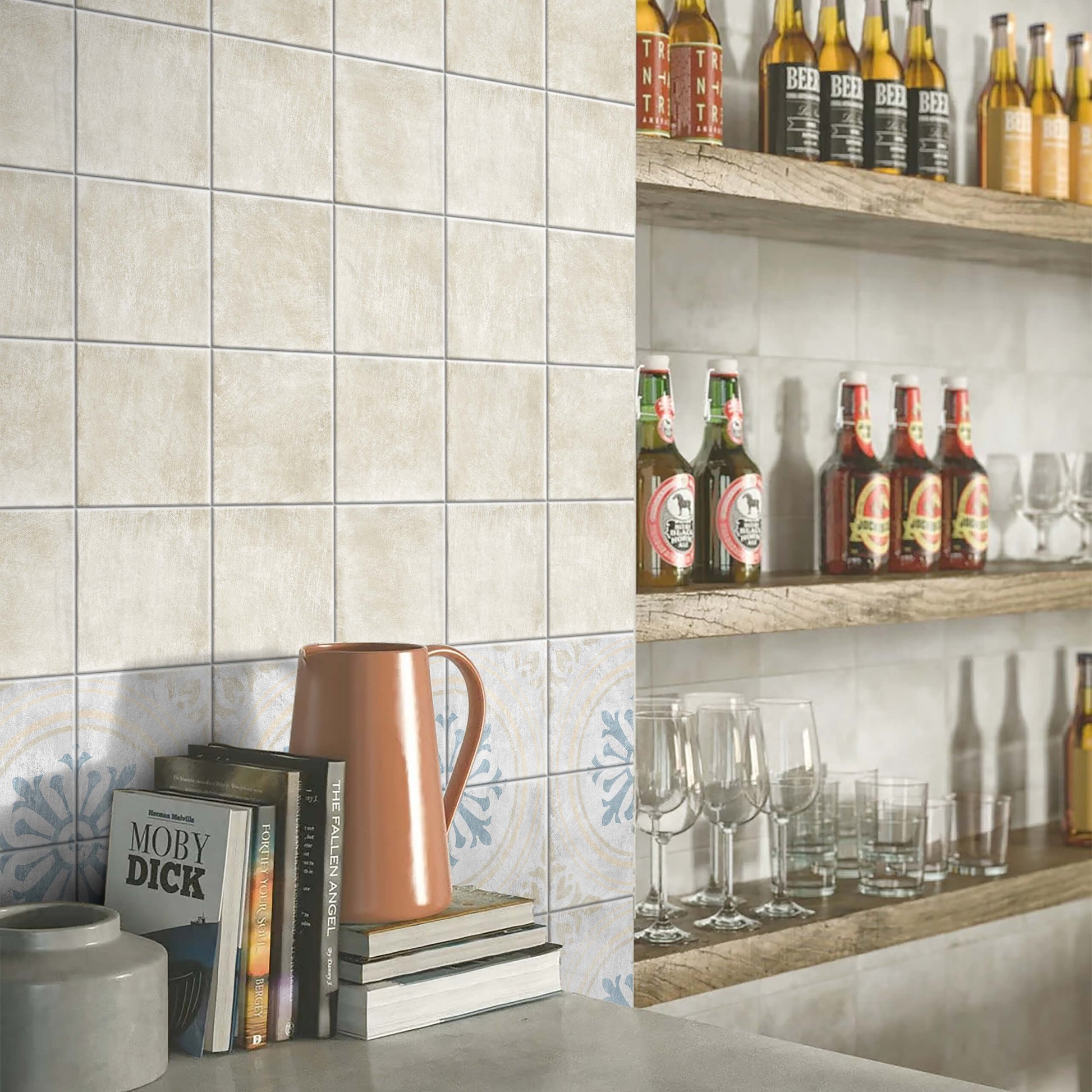 Antiquity Almond 150x150mm ceramic wall tiles installed in a bar setting with decorative patterned border tiles, wooden shelving, and glassware.