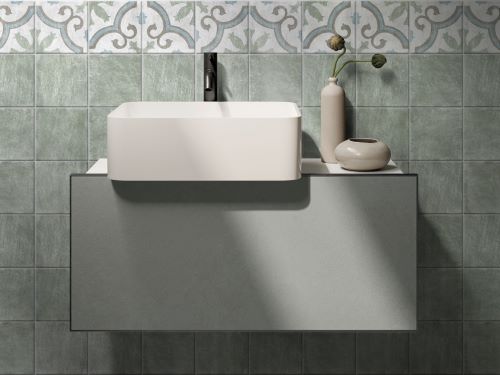 Antiquity Verde 150x150mm green ceramic wall tiles installed in a bathroom behind a white vessel sink on a floating grey vanity unit.