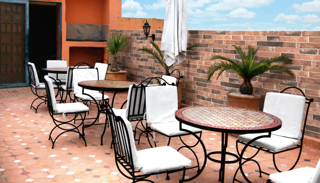 Argille Rame 160x400mm terracotta-toned tiles laid on a sunlit outdoor terrace patio with wrought-iron furniture, brick walls, and potted palms.