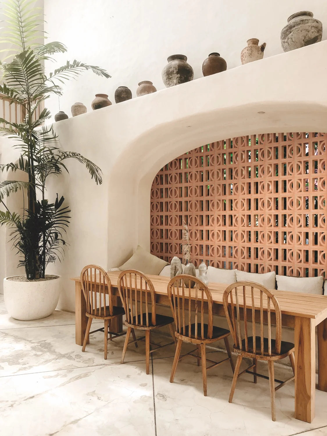 Artigianale Sole Breeze Blocks 150x150mm installed as a terracotta lattice screen within a curved white plaster arch niche, styled with a timber dining table and vintage ceramic pots.