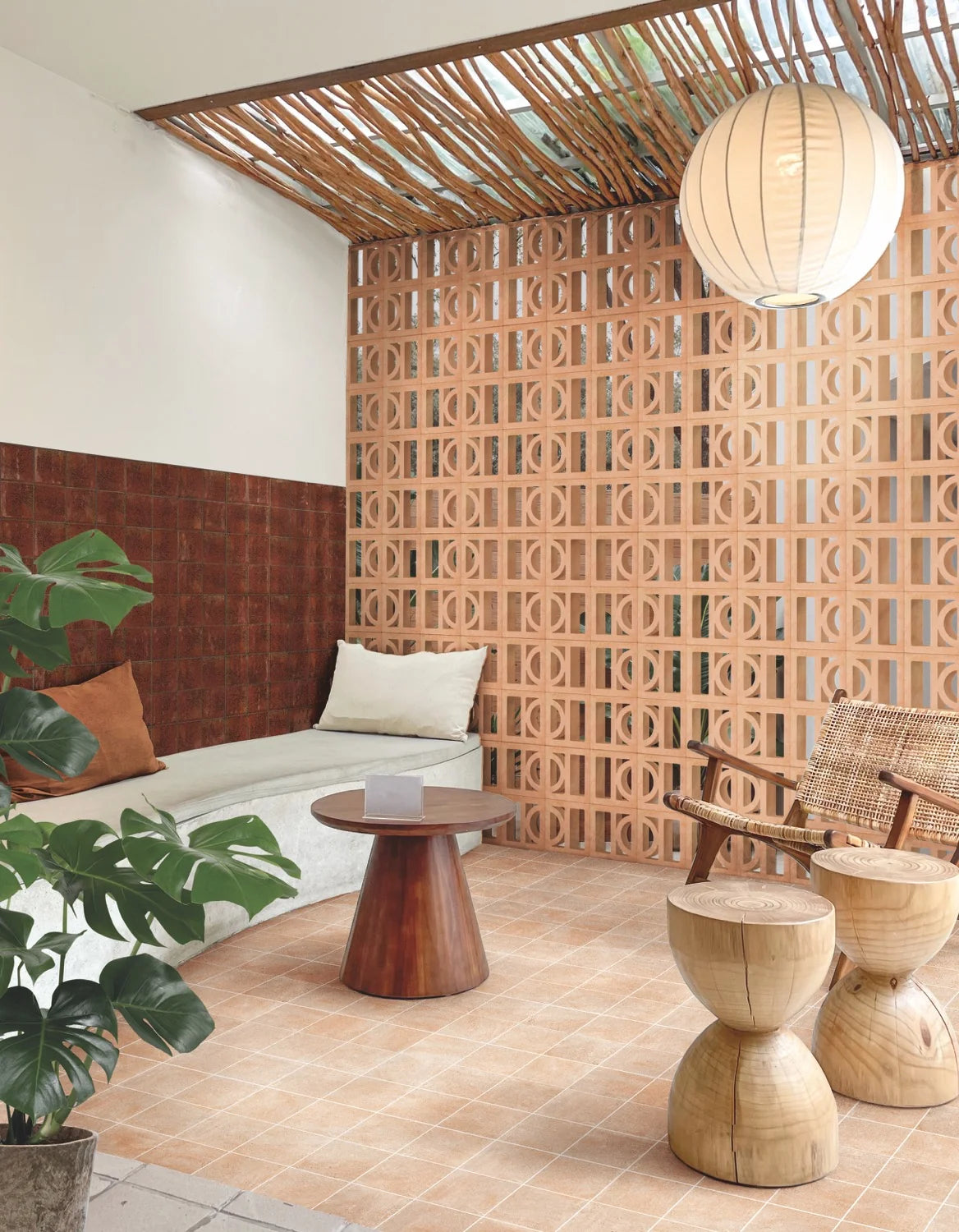 Artigianale Sole Breeze Blocks 150x150mm forming a terracotta lattice screen wall in a tropical lounge with a rattan chair, pendant light, and monstera plant.