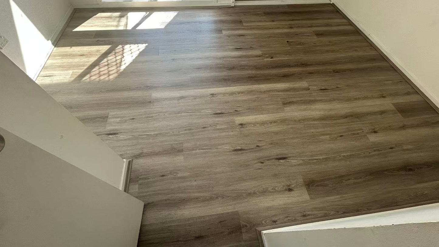 Ash Cliff Elegant SPC Hybrid 6.5mm Flooring 5+1.5mm installed in an empty sunlit bedroom, showcasing warm grey wood-look planks with natural oak texture and subtle knot details.