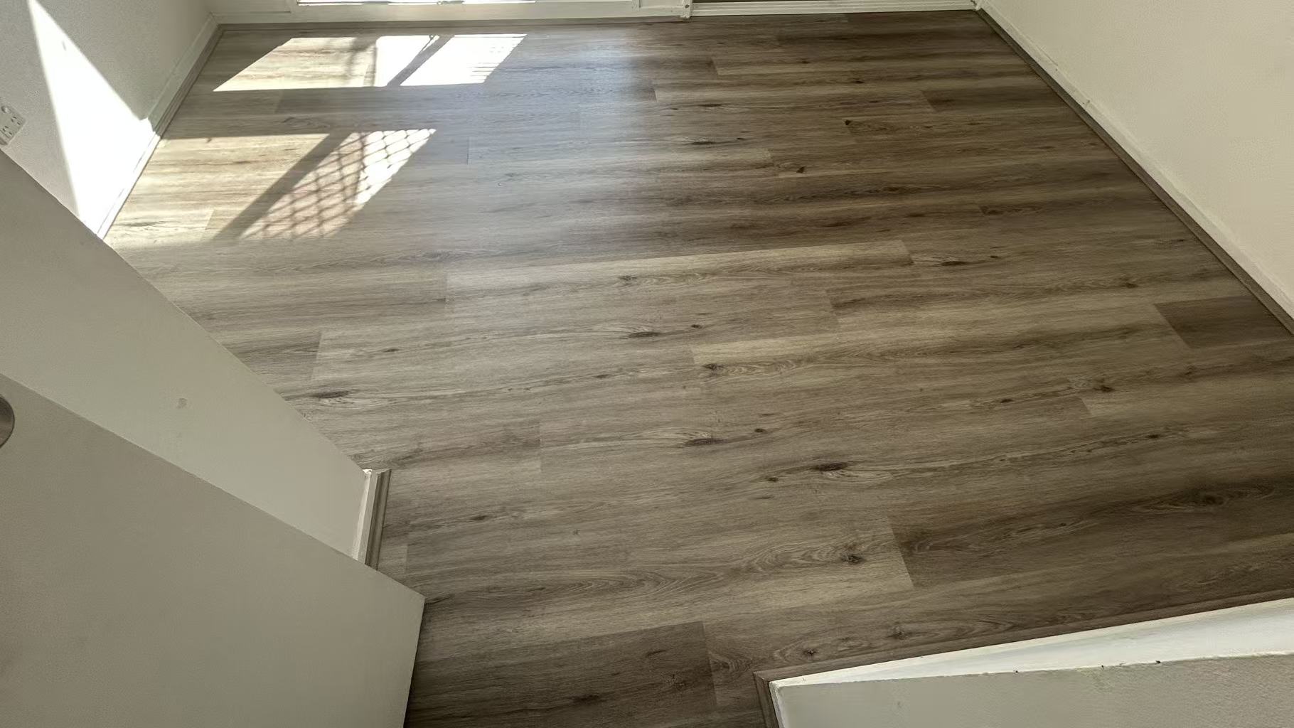 Ash Cliff Elegant SPC Hybrid 6.5mm Flooring 5+1.5mm installed in an empty sunlit bedroom, showcasing warm grey wood-look planks with natural oak texture and subtle knot details.