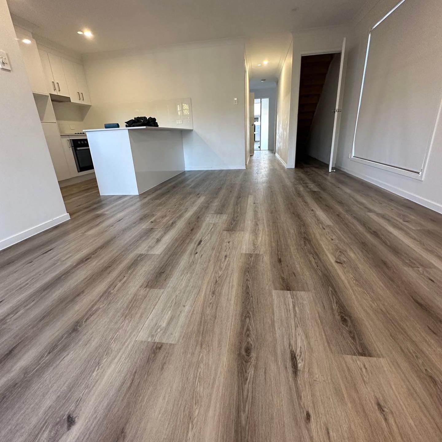 Ash Cliff Elegant SPC Hybrid 6.5mm Flooring 5+1.5mm installed across an open-plan living area featuring warm grey-brown wood-look planks, white kitchen island, and staircase beyond.