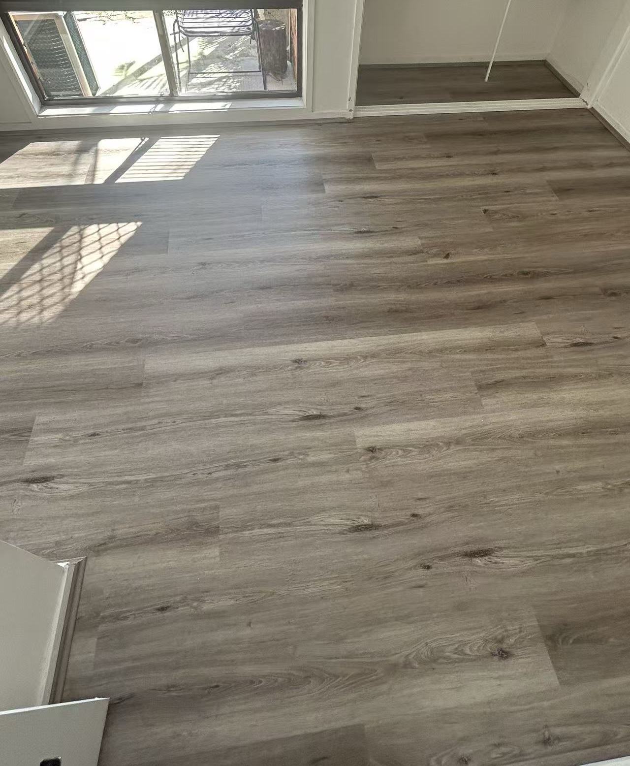 Ash Cliff Elegant SPC Hybrid 6.5mm Flooring 5+1.5mm installed in a sunlit open-plan living area with grey oak-look planks and sliding glass door.