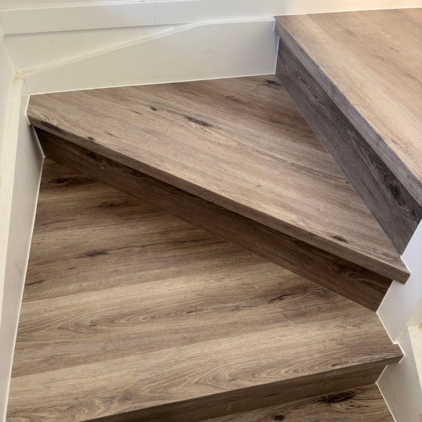 Ash Cliff Elegant SPC Hybrid 6.5mm Flooring 5+1.5mm installed on a winding staircase with warm grey-brown wood grain finish and white painted walls.