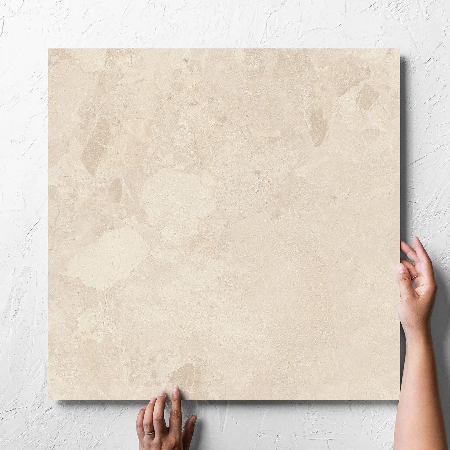 Hand holding a single Aurelia Stone Almond Grip 600x600mm tile against a white rendered wall, showing the matt surface