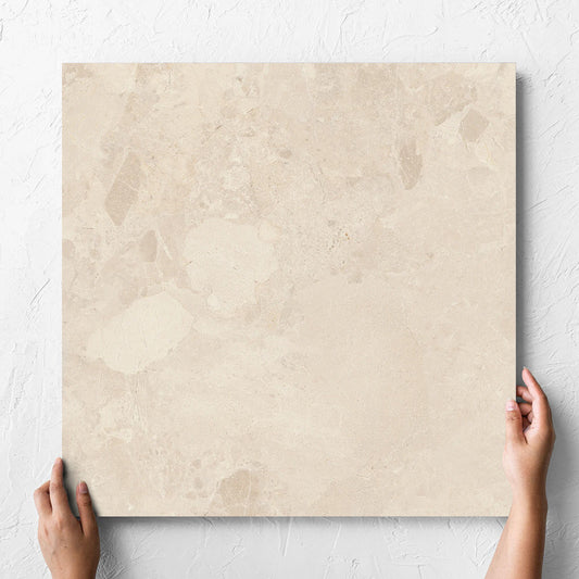 Hand holding a single Aurelia Stone Almond Matt 600x600mm tile against a white rendered wall, showing the matt surface