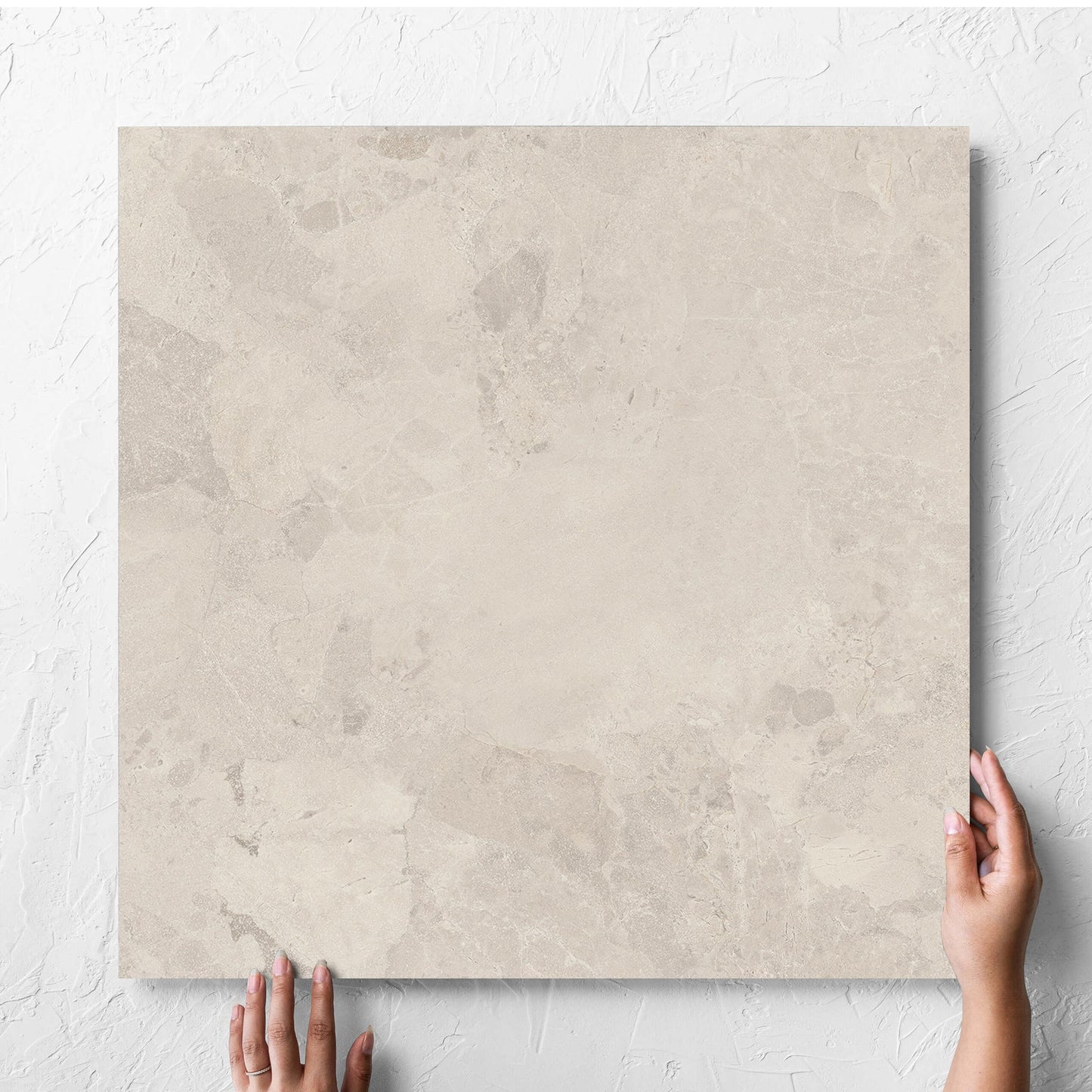 Hand holding a single Aurelia Stone Ash Grip 600x600mm tile against a white rendered wall, showing the matt surface