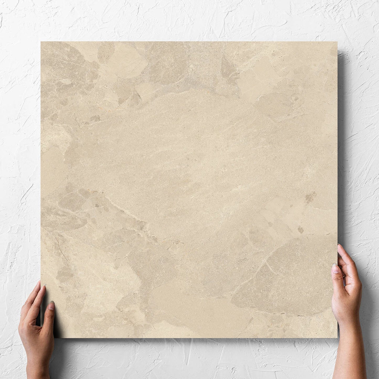 Hand holding a single Aurelia Stone Beige Grip 600x600mm tile against a white rendered wall, showing the matt surface