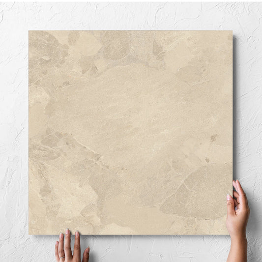 Hand holding a single Aurelia Stone Beige Matt 600x600mm tile against a white rendered wall, showing the matt surface