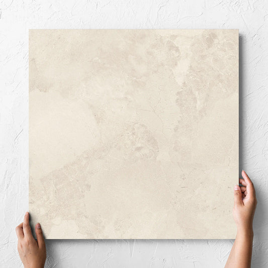 Hand holding a single Aurelia Stone White Matt 600x600mm tile against a white rendered wall, showing the matt surface