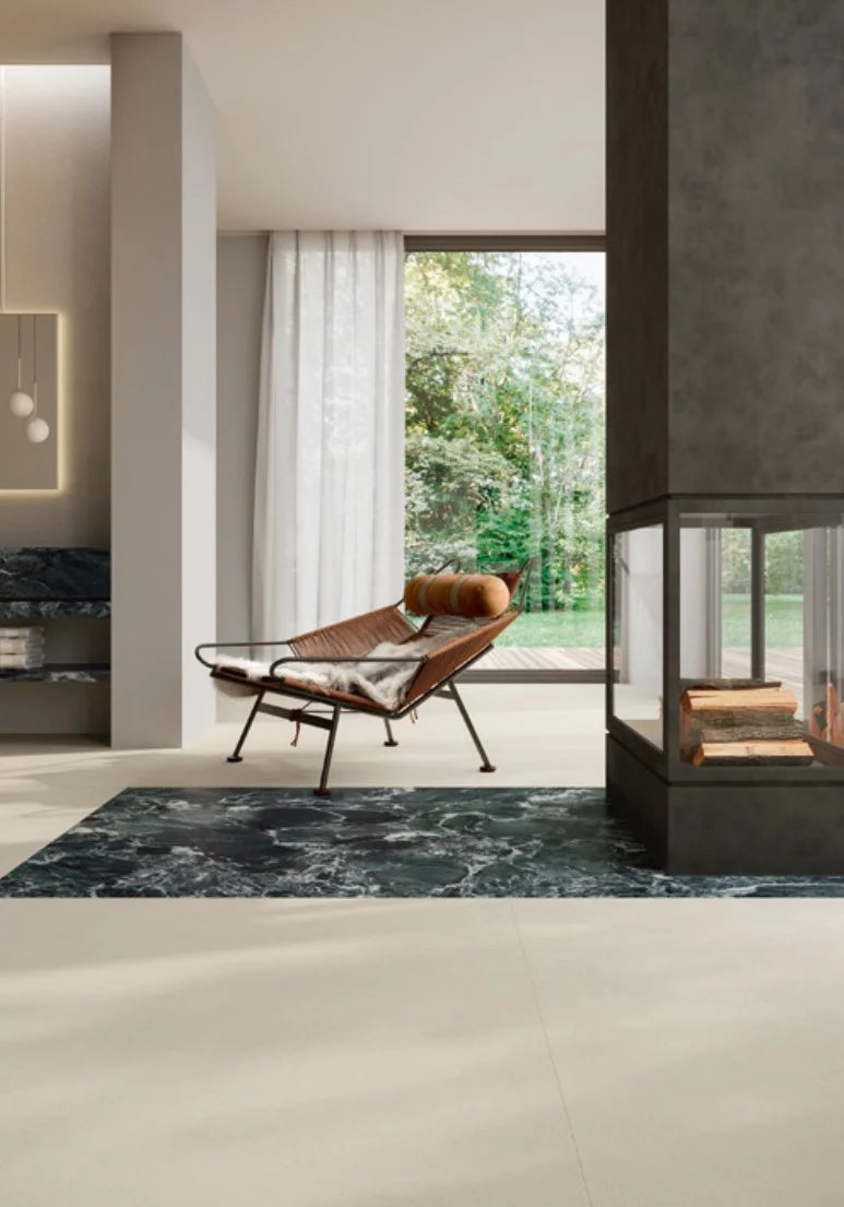 Balance Ivory Matt 600x1200mm porcelain tiles laid on a spacious living room floor complemented by a dark marble inset rug area, lounge chair, and glass fireplace.