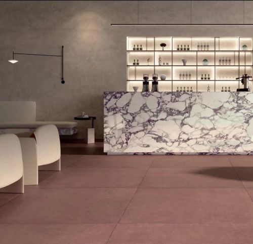Balance Marsala Red 600x600mm tiles installed as a warm dusty-rose floor in a modern cafe bar setting with a marble reception counter and illuminated shelving backdrop.