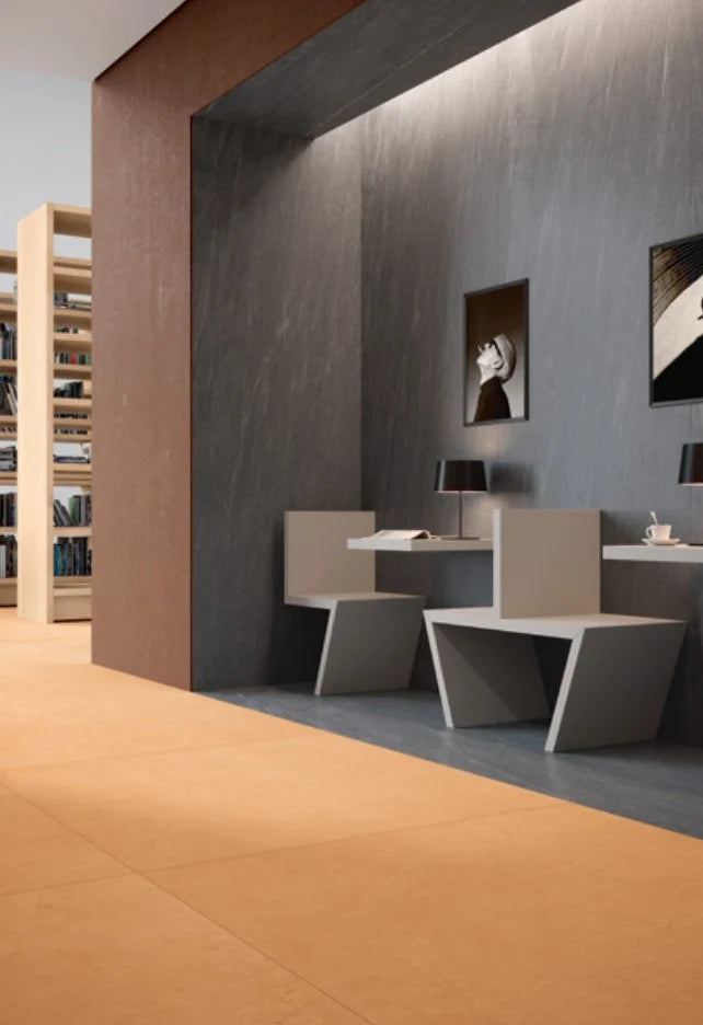 Balance Orange Matt 600x600mm floor tiles installed in a modern library reading nook with dark stone walls, geometric chairs, and built-in bookshelves.