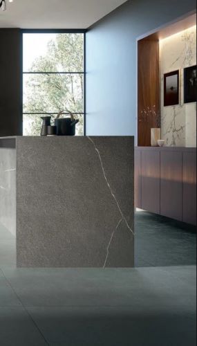 Balance Steel Blue Mat 600x600mm porcelain tile cladding a dramatic kitchen island with subtle white veining, dark vases, and warm timber cabinetry in the background.