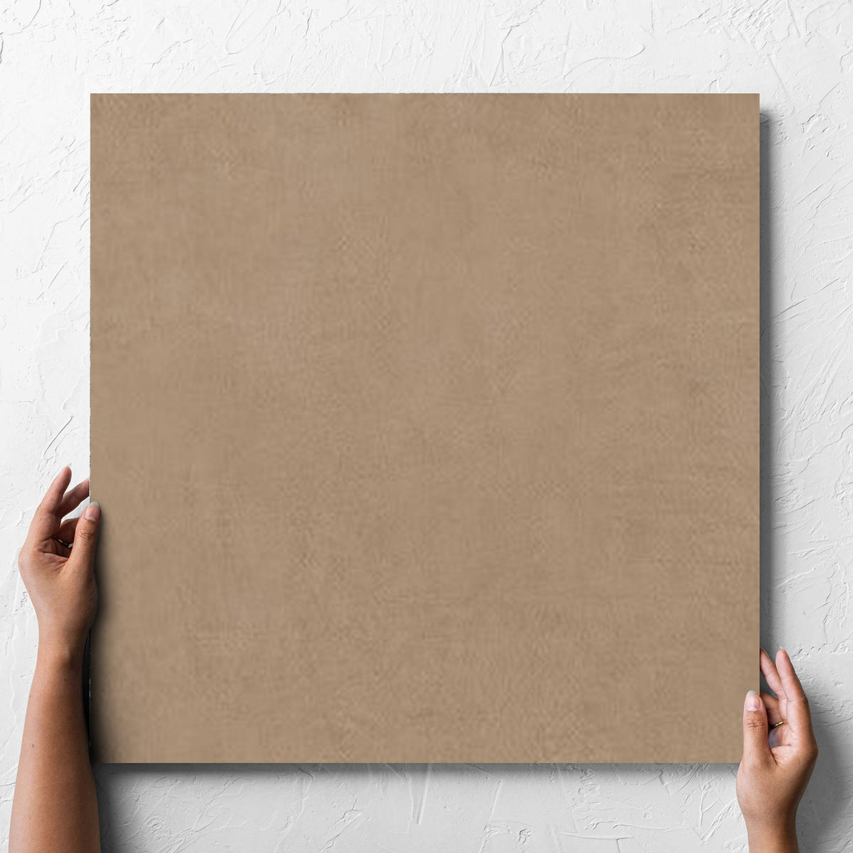 Hand holding a single Balance Tan Matt 600x600mm tile against a white rendered wall, showing the tile surface